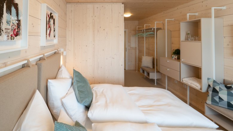 Modernes Doppelzimmer mit Holzwänden, Bett, Kissen und minimalistischer Einrichtung.