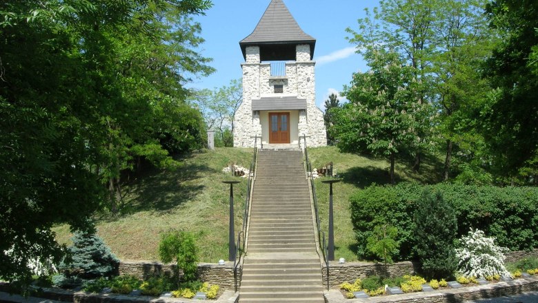 Steinturm auf einem Hügel mit Treppe und grüner Umgebung.