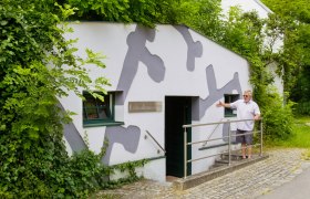 Eingang des Erdstallmuseums Althöflein mit einem Mann, der die Tür zeigt.