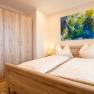 Ein gem&uuml;tliches Schlafzimmer mit einem Doppelbett, Holzm&ouml;beln und einem bunten Gem&auml;lde an der Wand.