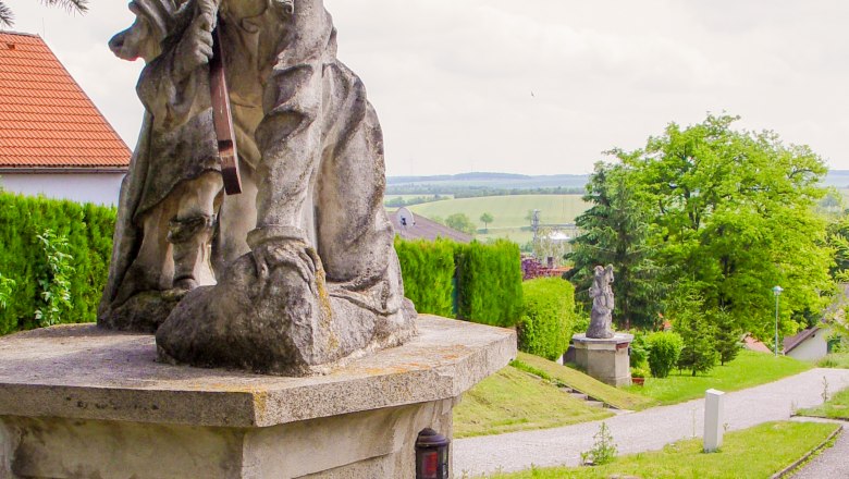 Steinstatue auf einem Sockel mit gr&uuml;ner Landschaft im Hintergrund.