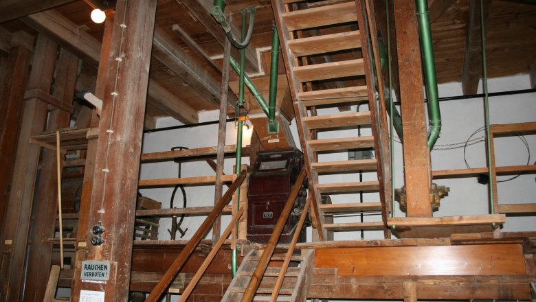 Innenansicht einer alten M&uuml;hle mit Holztreppen und Maschinen.