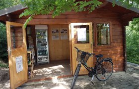 Kleines Holzhaus mit offenem Eingang, K&uuml;hlschrank mit Getr&auml;nken und einem Fahrrad davor.