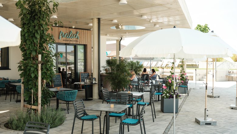 Außenbereich eines Cafés mit Tischen, Stühlen und Sonnenschirmen.