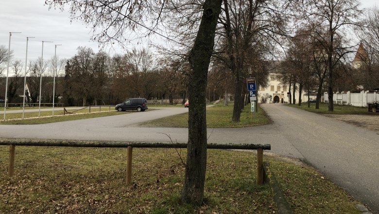 Parkplatz mit Bäumen und einem Gebäude im Hintergrund.