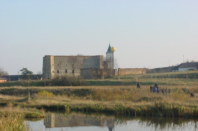 Ruine mit Turm und goldener Kugel in einer l&auml;ndlichen Landschaft mit Teich im Vordergrund.