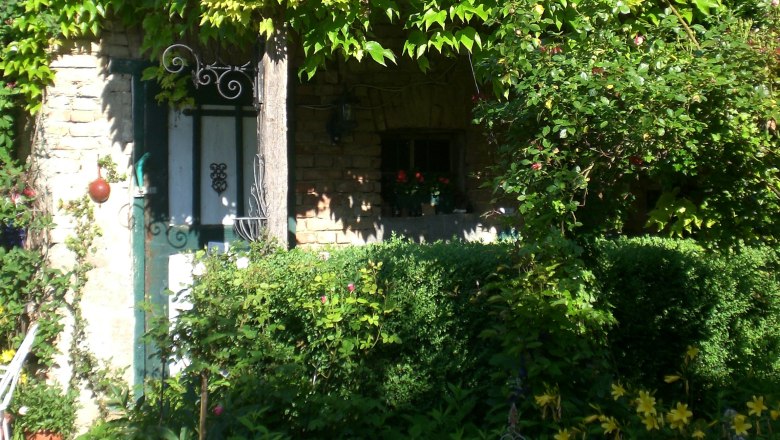 Ein idyllischer Landhausgarten mit üppigem Grün und Blumen vor einem alten Steinhaus.