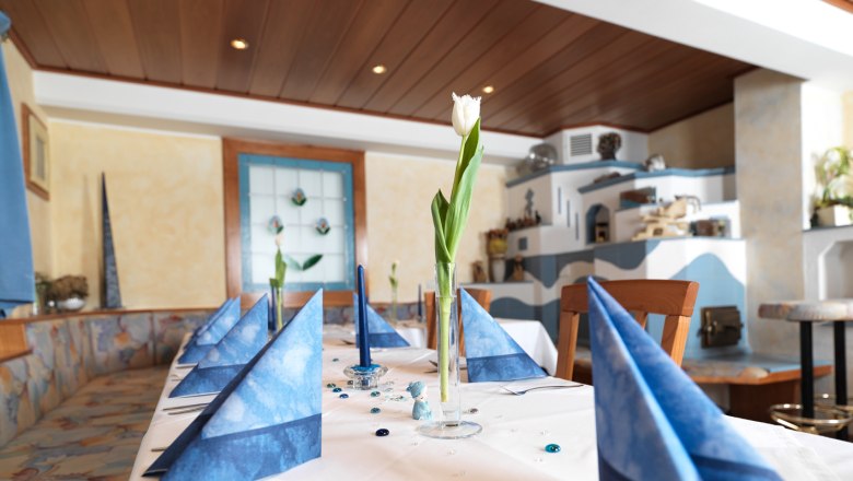 Ein elegant gedeckter Tisch mit blauen Servietten und einer weißen Tulpe in einem Glas in einem gemütlichen Raum.