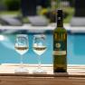 Eine Flasche Wein und zwei Weingl&auml;ser auf einem Holztisch vor einem Pool.