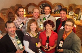 Gruppe von Menschen in einer Vinothek, die Weinflaschen halten.