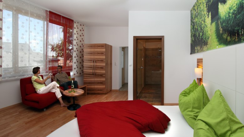 Modernes Gästezimmer mit rotem Sofa, grün-rotem Bett und großem Fenster.
