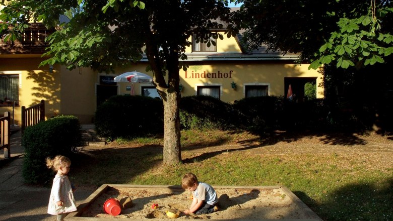 Zwei Kinder spielen im Sandkasten vor einem Gebäude mit der Aufschrift 'Lindenhof'.