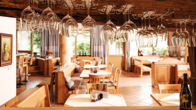 Innenansicht eines Restaurants mit hängenden Weingläsern und Holzmöbeln.