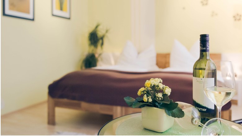 Ein gemütliches Schlafzimmer mit einem Bett im Hintergrund und einem Tisch mit einer Weinflasche und einem Glas im Vordergrund.