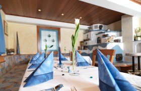 Ein elegant gedeckter Tisch mit blauen Servietten und einer weißen Tulpe in einem Glas in einem gemütlichen Raum.