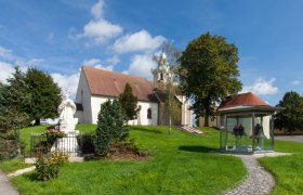 Wehrkirche St. Stephan mit Statue und Glockenhäuschen im Vordergrund.
