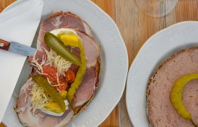 Zwei Teller mit belegten Broten und zwei Gläser Weißwein auf einem Holztisch.