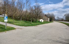 Parkplatz mit Wohnmobilstellplatzschild, Bäume und altes Gebäude im Hintergrund.