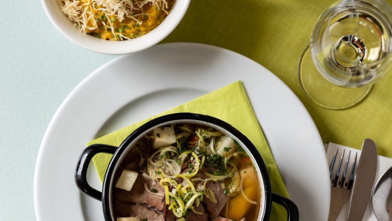 Ein Tisch mit einem Teller Suppe, einer Schüssel Brei mit Käse, einem Glas Wasser und Besteck auf einer grünen Serviette.