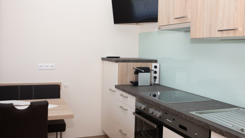 Moderne Küche mit Herd, Spüle, Kaffeemaschine und Wandfernseher.