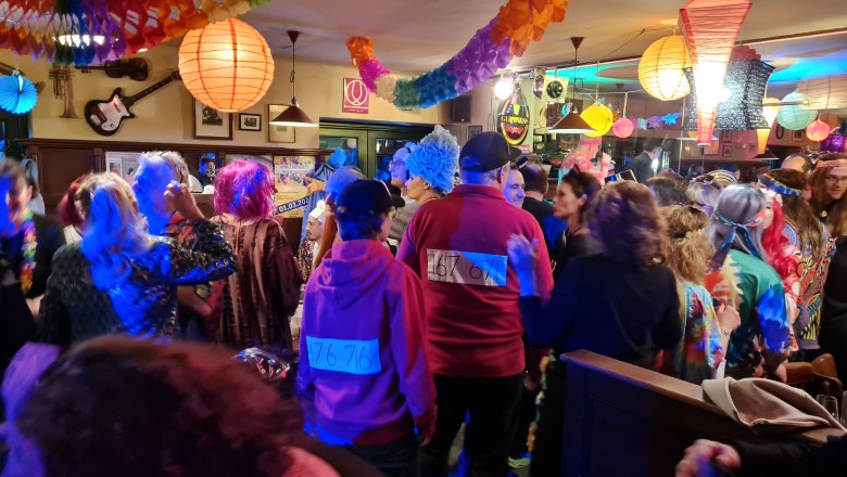 Menschen in bunten Kostümen feiern Fasching in einem dekorierten Raum.