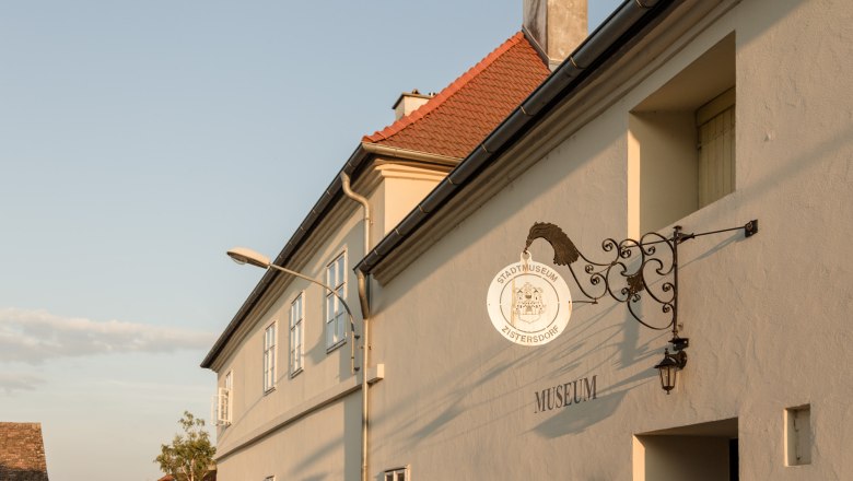 Au&szlig;enansicht des Stadtmuseums Zistersdorf mit einem dekorativen Schild und einem Laternenpfahl im Vordergrund.