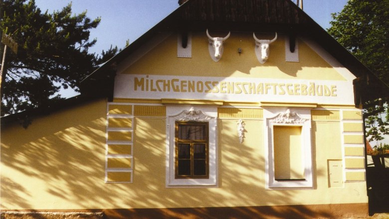 Ein gelbes Geb&auml;ude mit der Aufschrift 'Milchgenossenschaftsgeb&auml;ude' und zwei Stiersch&auml;deln an der Fassade.