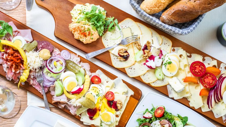 Verschiedene Aufschnitt- und Käseplatten mit Brot und Salat auf einem Tisch.