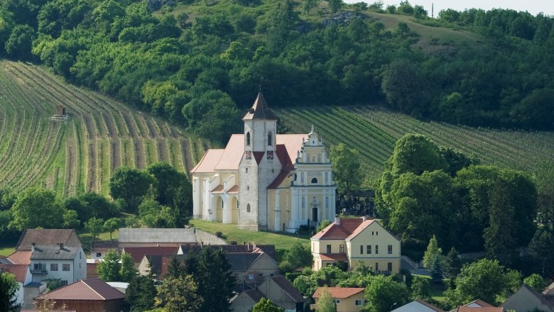Eine Kirche inmitten von Weinbergen und Häusern, umgeben von grünen Hügeln.