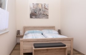 Schlafzimmer mit Doppelbett, Holzmöbeln und abstraktem Kunstwerk an der Wand.