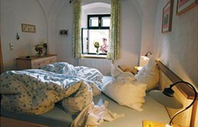 Gem&uuml;tliches Schlafzimmer mit ungemachtem Bett und Blick aus dem Fenster auf eine Person mit Blumen.