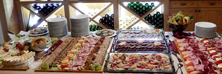 Buffet mit verschiedenen Fleisch- und Käseplatten vor einem Weinregal.
