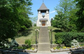 Steinturm auf einem Hügel mit Treppe und grüner Umgebung.