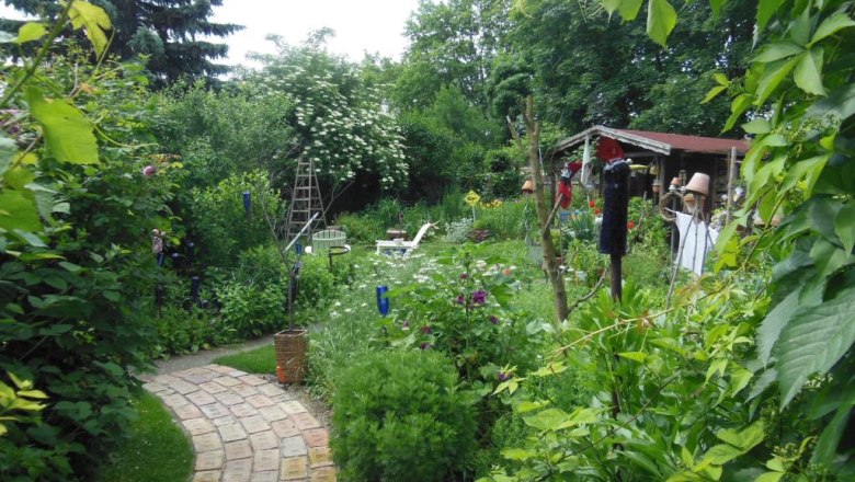 Ein üppiger Garten mit einem geschwungenen Ziegelweg, umgeben von Bäumen und Sträuchern, mit einer kleinen Hütte im Hintergrund.