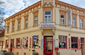 Außenansicht des Cafe Restaurant Harlekin mit gelber Fassade und roten Fenstern.