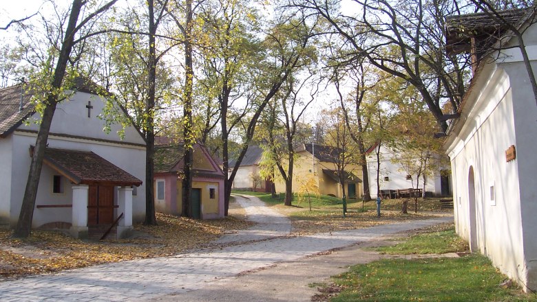 Ein ruhiger Dorfplatz mit kleinen, traditionellen Gebäuden und Bäumen im Herbst.