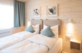 Gemütliches Doppelzimmer mit zwei Einzelbetten, Holzwänden und moderner Dekoration.