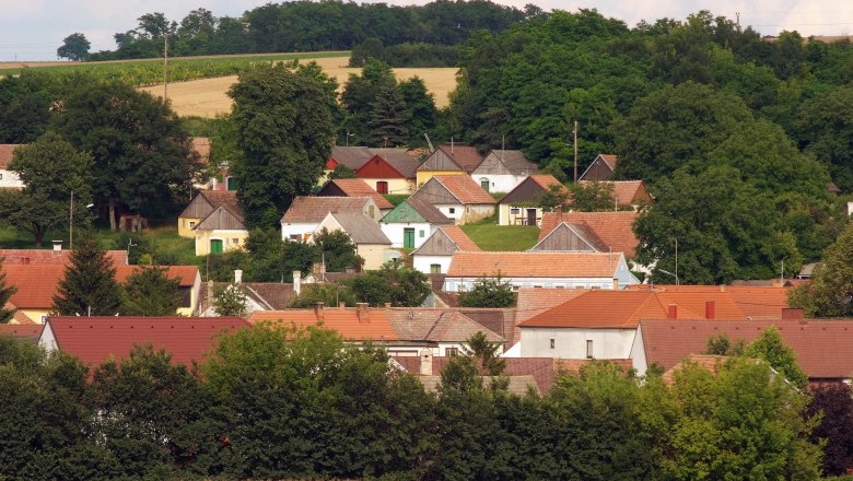 Blick auf ein Dorf mit bunten Häusern und grüner Landschaft im Hintergrund.