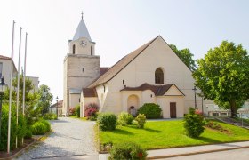Eine Kirche mit einem Turm und Uhr, umgeben von einem gepflegten Garten und B&auml;umen.