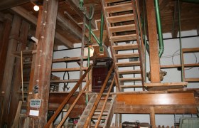Innenansicht einer alten Mühle mit Holztreppen und Maschinen.