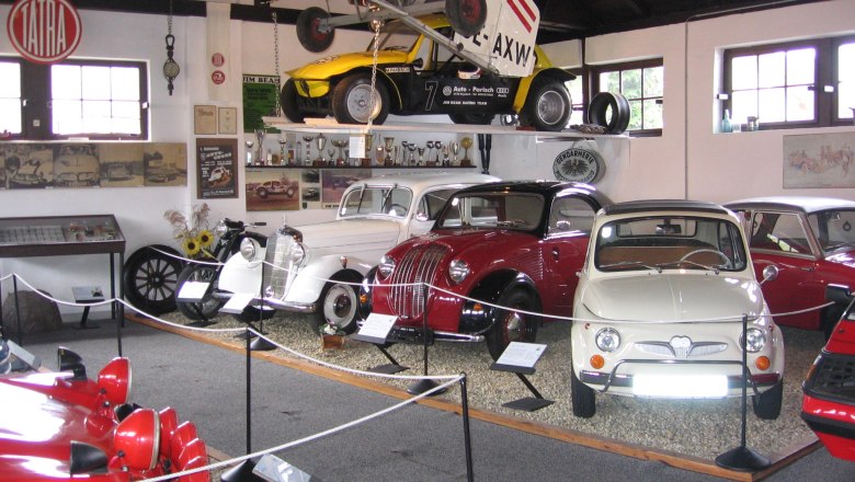 Innenansicht eines Oldtimermuseums mit verschiedenen klassischen Autos und einem Flugzeug an der Decke.