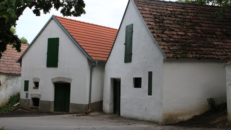 Zwei traditionelle Weinkeller mit weißen Wänden und roten Ziegeldächern in einer Kellergasse.