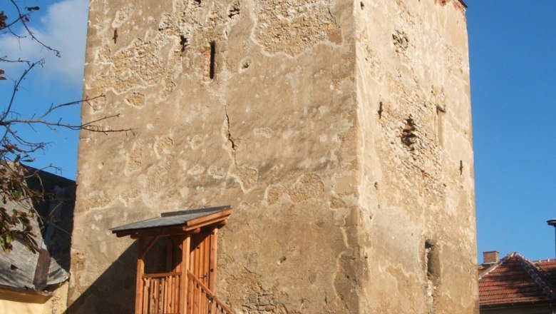 Ein alter Wehrturm mit h&ouml;lzerner Treppe und Gel&auml;nder, umgeben von Geb&auml;uden, unter blauem Himmel.